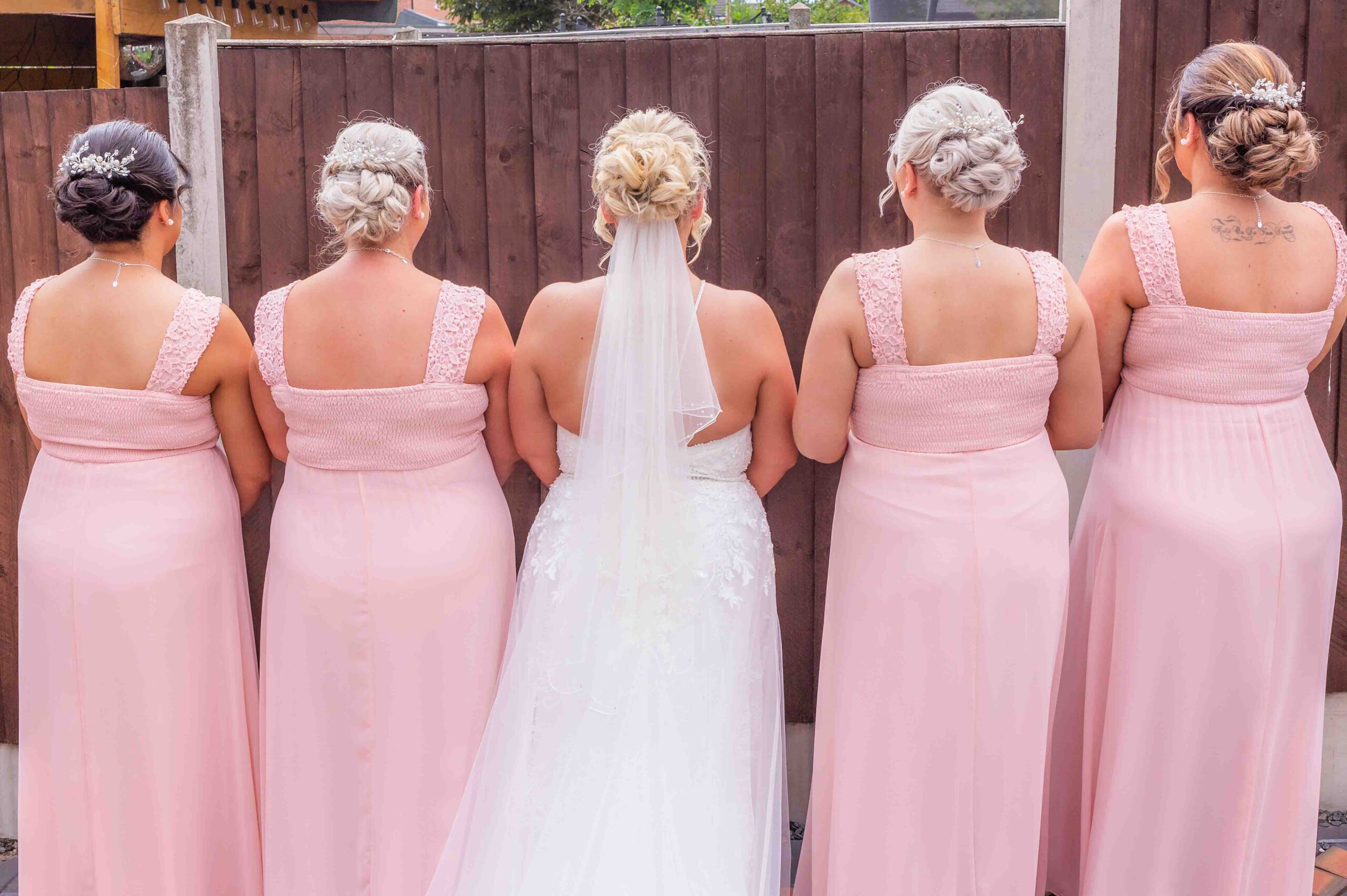 Four bridemaids in pink dresses and a bride in a white in a photograph with their backs turned