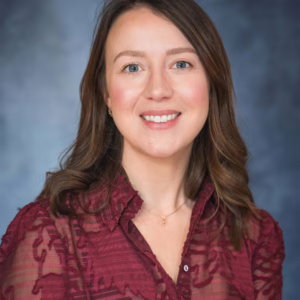 A white lady with brown hair and blue eyes smiling for a corporate headshot with a deep blue background